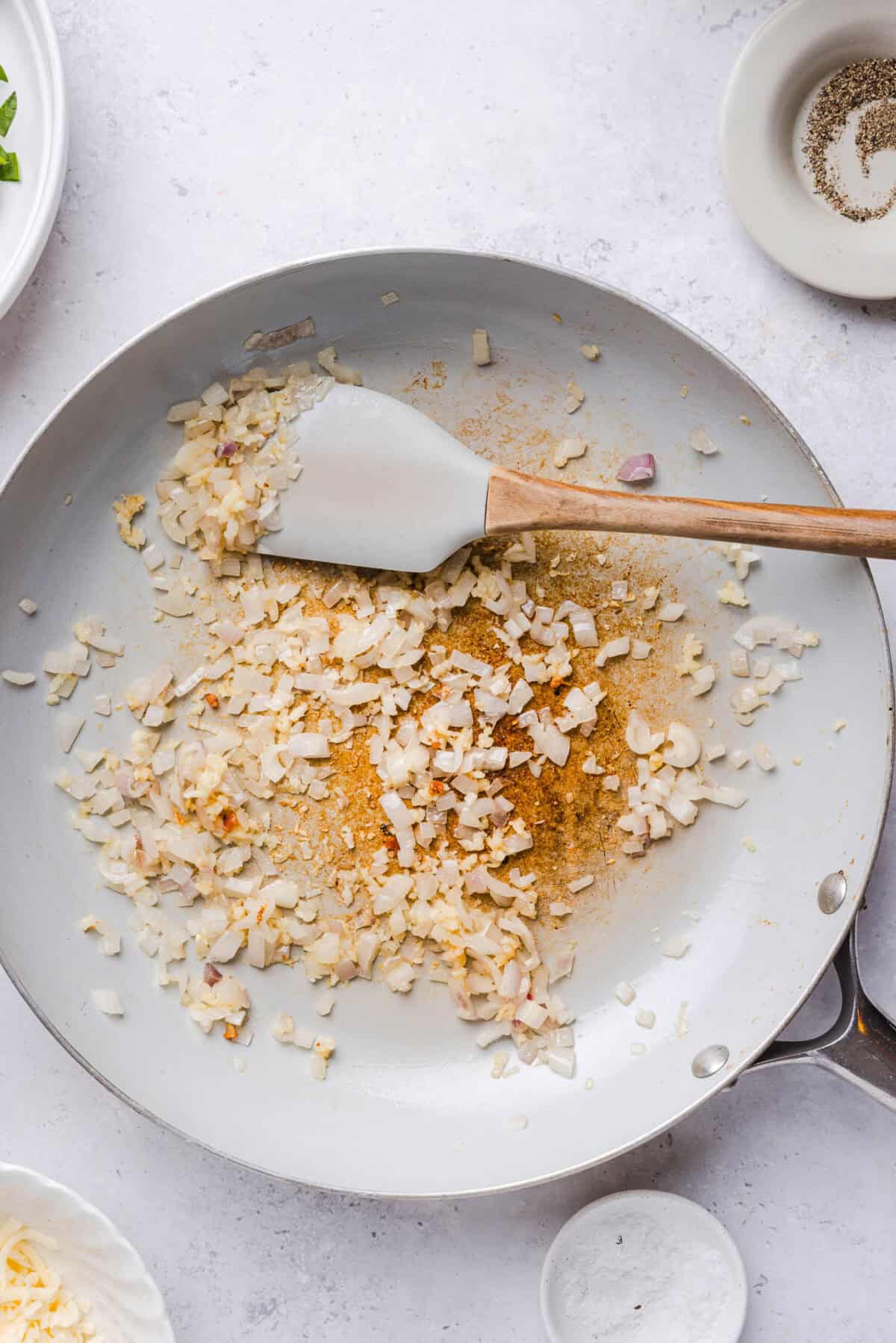 Sautéing minced garlic and shallots in a white skillet with a spatula