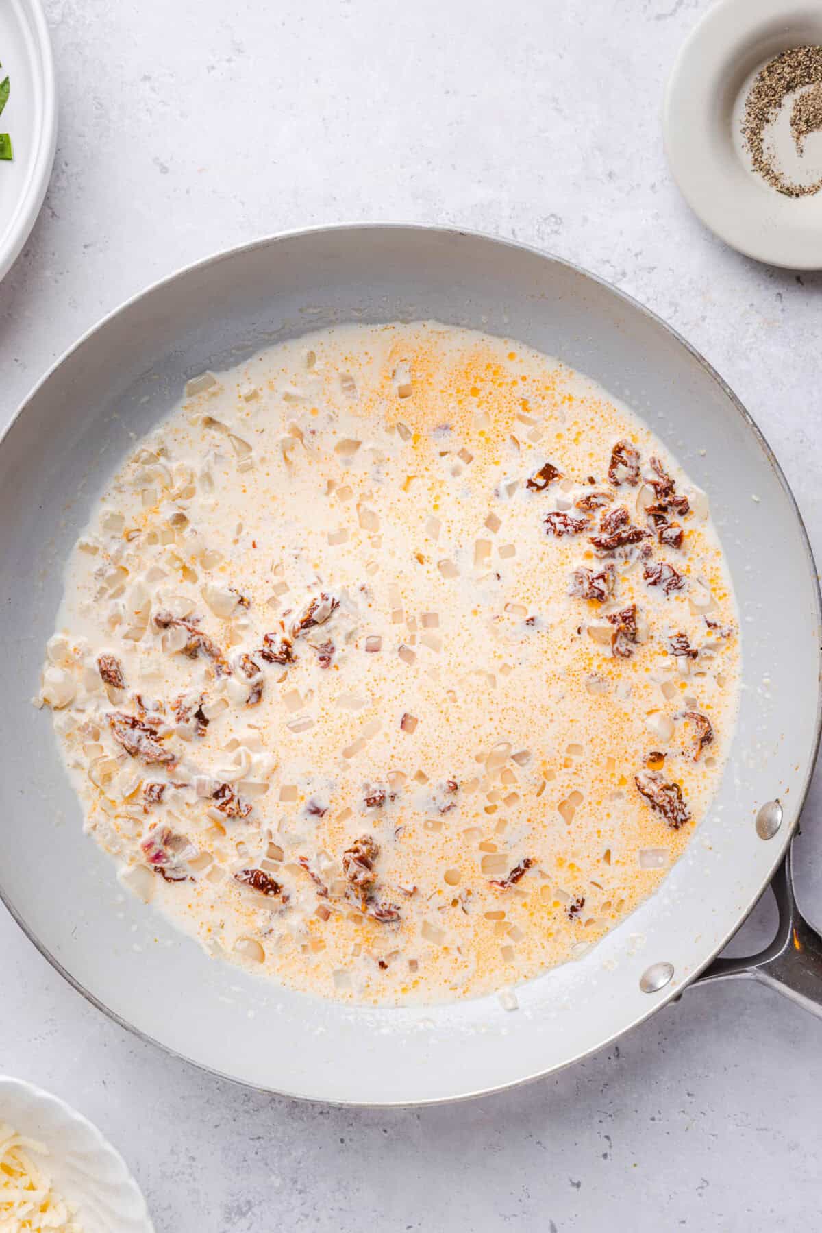 Cream and sun-dried tomatoes simmering together in a white skillet for marry me sauce