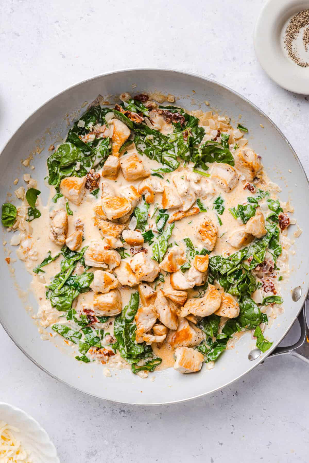 Seared chicken pieces stirred into creamy marry me sauce with wilted spinach in a skillet