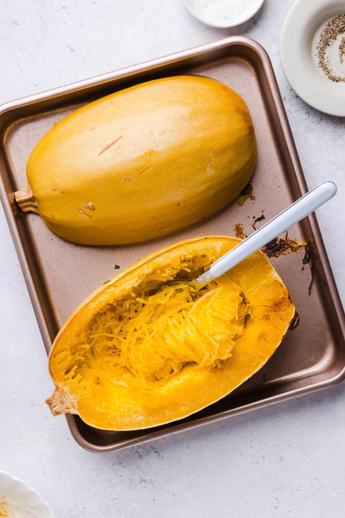 Fork scraping roasted spaghetti squash into strands on a baking sheet